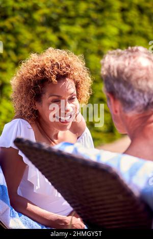 Rentnerpaar, Das Sich Auf Liegestühlen Unterhielt, Um Sich Im Sommerurlaub Am Pool Zu Entspannen Stockfoto