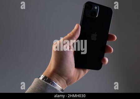 Die Hand eines Mannes an einer grauen Wand hält ein modernes schwarzes iPhone 13 Smartphone in den Händen Stockfoto