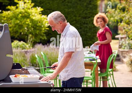 Seniorenpaar Kocht Grill Im Freien Und Bereitet Tisch Für Die Dinner Party Zu Hause Vor Stockfoto