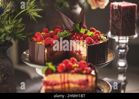 Stillleben von leckeren geschichteten Mousse Kuchen mit geschmolzener Schokolade Belag mit Himbeeren verziert Stockfoto