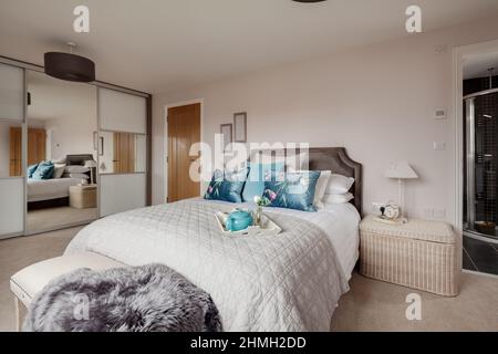 Newport, Essex - März 21 2019: Luxuriöse moderne Master-Schlafzimmer-Suite mit verspiegelten Kleiderschränken, Tür offen zum eigenen Bad und einem gekleideten Bett. Stockfoto