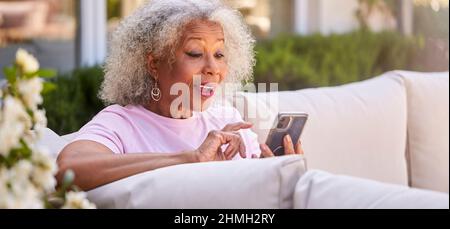 Ältere Frau Im Ruhestand, Die Draußen Im Garten Zu Hause Sitzt Und Videoanrufe Auf Dem Mobiltelefon Führt Stockfoto