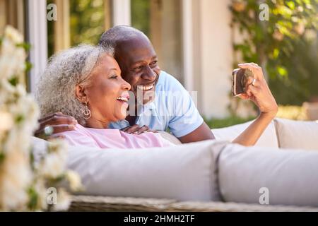 Rentnerpaar Sitzt Draußen Im Garten Zu Hause Und Macht Videoanruf Auf Dem Mobiltelefon Stockfoto