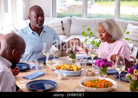 Multi Generation Family Hält Sich Zu Hause Am Tisch Und Sagt Grace, Bevor Sie Zusammen Essen Stockfoto