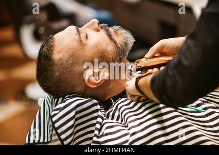Der Friseur trimmt den Bart des Kunden in seinem Friseursalon in einem Beauty- und Pflegekonzept Stockfoto