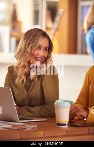 Weibliche Geschäftskollegen Mit Laptop, Die Sich In Einem Büro-Café Um Den Tisch Treffen Stockfoto