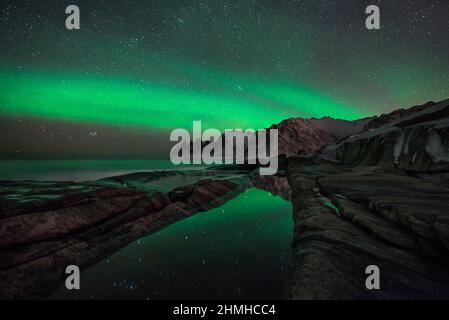 Aurora Borealis über den Devils Jaw Mountains spiegelt sich in einem natürlichen Wasserbecken wider, Tungeneset, Senja, Norwegen Stockfoto