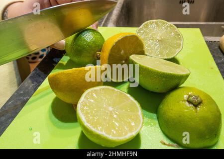 Schneiden Sie Zitronen und Limetten mit einem Küchenmesser auf einem grünen Schneidebrett Stockfoto