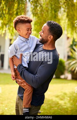 Liebevoller Vater Hält Lächelnden Sohn In Den Armen Im Garten Zu Hause Stockfoto