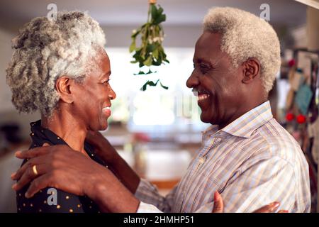 Liebevolles Senior-Paar Unter Mistelzweig Feiert Weihnachten Zu Hause Zusammen Stockfoto