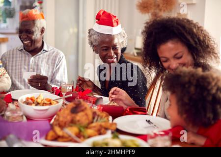 Multi Generation Family In Paper Hats Lesen Weihnachten Cracker Witze Vor Dem Essen Zusammen Stockfoto