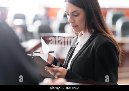 Brunette Staatsanwaltschaft Lesung Klage in der Nähe verschwommen Richter im Gerichtssaal Stockfoto