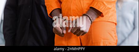 Beschnittene Ansicht eines afroamerikanischen Mannes mit Handschellen in Gefängnisuniform auf verschwommenem Hintergrund, Transparent Stockfoto