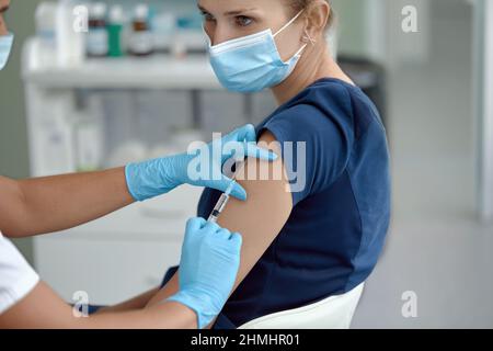 Ärztin mit Spritze, die eine Impfdosis von 19 Covid in der Schulter einer weiblichen Patientin verabreichte. Konzept für klinische Studien zum Grippeimpfstoff, Stockfoto