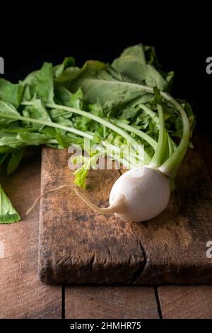 Frischer weißer Rettich mit Blättern, essbares und gesundes Wurzelgemüse auf Holzbrett, dunkler Hintergrund mit Kopierraum, rustikales Konzept Stockfoto