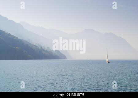 Herbstnebel über dem See. Silhouetten von Bergen im Hintergrund. Einsames Segeln. Stockfoto