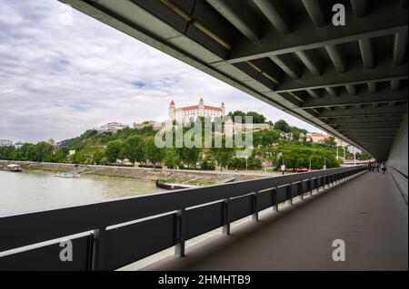 BRATISLAVA, SLOWAKEI - 9. JULI 2019: Blick auf den Fußweg auf die meisten SNP-Brücken mit der Burg Bratislava und der Donau im Hintergrund Stockfoto