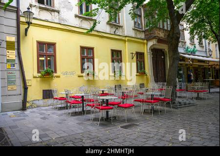 BRATISLAVA, SLOWAKEI - 9. JULI 2019: Leere Tische und Stühle in einem baumbestandenen Essbereich im Freien in Bratislava Stockfoto