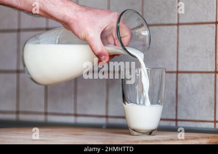 Die Hand eines Mannes hält einen Krug und gießt Milch in ein Glas Stockfoto