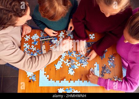 Draufaufnahme Der Familie, Die Zu Hause Um Den Tisch Sitzt Und Zusammen Puzzle Macht Stockfoto