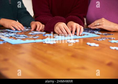 Nahaufnahme Der Familie, Die Zu Hause Am Tisch Sitzt Und Zusammen Puzzle Macht Stockfoto