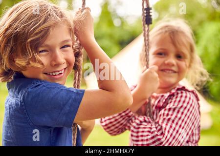 Portrait Von Zwei Kindern, Die Im Garten Zu Hause Auf Swing Spielen Stockfoto