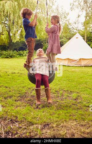 Drei Kinder Spielen Auf Reifen Swing Im Garten Zu Hause Mit Zelt Im Hintergrund Stockfoto