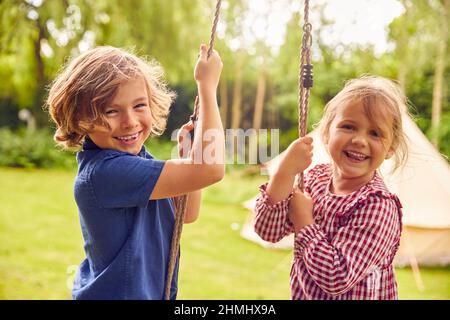 Portrait Von Zwei Kindern, Die Im Garten Zu Hause Auf Swing Spielen Stockfoto