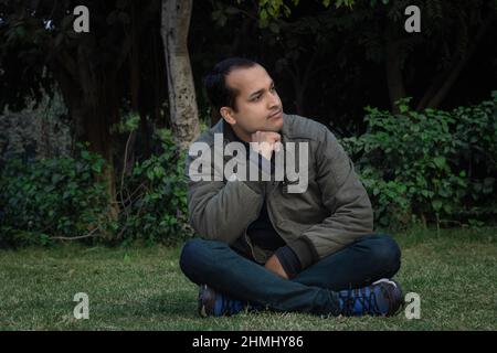 Junger Mann verschiedene Stimmungen des Ausdrucks Kreuz Bein sitzt in einem Park aus flachem Winkel Stockfoto