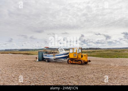 Fischerboot auf einem Anhänger, der von einem Raupendozer auf einem Kiesstrand, Cley-Next-the-Sea, einem Küstendorf in Norfolk, East Anglia, England, gezogen wird Stockfoto