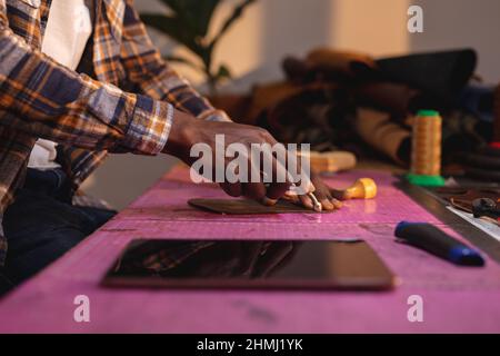 Mittelteil eines afroamerikanischen jungen Handwerkers, der in der Werkstatt Leder auf Matte schneidet Stockfoto