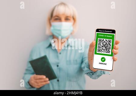 Covid-19-Steuerung. 50s kaukasische Frau in Maske hält Smartphone mit digitalem grünen Pass und QR-Code auf dem Bildschirm. Gesundheitspass oder Bescheinigung von Stockfoto