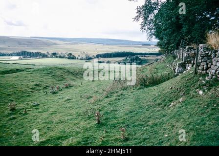 Bremenium - ein altes römisches Fort (Castrum) in Rochester, Northumberland, England. Die Festung war eine der Verteidigungsstrukturen entlang der Dere Street, einer römischen Straße, die von York nach Corbridge und weiter nach Melrose führt. Südwand Gräben und Intervall Turm. Archivscan von einem Dia. Oktober 1974. Stockfoto