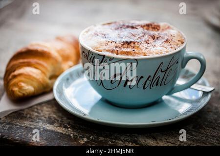 Schaumige Tasse heiße Schokolade mit einer Prise Kakaopulver auf einer rustikalen Holzarbeitsfläche Stockfoto