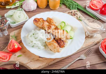 Gebratener lula Kebab auf Pita-Brot mit Zwiebeln und Gemüse auf einem weißen Teller auf dunklem Holzgrund Stockfoto