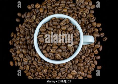 Weiße Tasse mit Kaffeebohnen auf schwarzem Hintergrund isoliert angeordnet Stockfoto