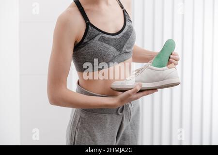 Fitness Frau in Sportbekleidung mit orthopädischen Einlagen und Sneakers. Frau, die zu Hause aus nächster Nähe orthopädische Einlegesohle in den Schuh setzt. Banner zur Fußpflege. Flach Stockfoto