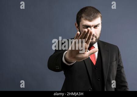 Ein Mann in einem Anzug hält seine Handfläche vor einem grauen Hintergrund aus. Stopp-Signal. Stopp. Hand-Stopp-Schild. Handbewegung Stockfoto