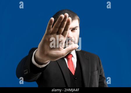 Ein Mann in einem Anzug hält seine Handfläche vor einem blauen Hintergrund aus. Stopp-Signal. Stopp. Hand-Stopp-Schild. Handbewegung Stockfoto