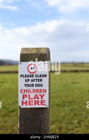 Ein Schild, das an einem Pfosten befestigt ist und Hundebesitzer und Hundespaziergänger auffordert, jegliches Chaos zu beseitigen oder ihre Hunde zu bescheuern, kann in einem Bereich, in dem Kinder spielen, auftreten. Stockfoto