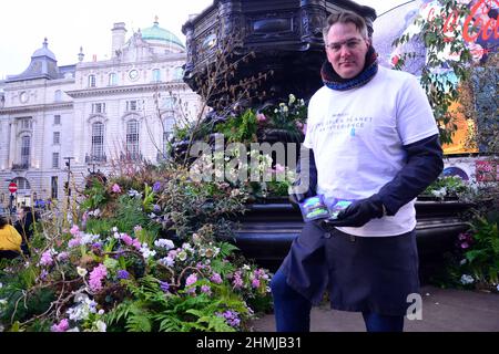 Pflanzen und Blumen bedecken den Shaftesbury Memorial Fountain, der oft als „Eros“ bekannt ist, im Piccadilly Circus, London, England, Großbritannien. Dies wirbt für eine Green Planet Augmented Reality Experience, die am 11th. Februar 2022 im Piccadilly Circus eröffnet wird. Partner und Unterstützer des Projekts sind BBC Earth, EE, Crown Estate, Factory 42, Kew Royal Botanic Gardens, Talesmith und Dimension. Das Projekt bietet die Online-Buchung von Freikarten an und läuft bis zum 9th. März 2022. Adam, ein Botschafter des Projekts, steht vor der Statue, bereit, die Passanten zu informieren und Samen zu verschenken. Stockfoto