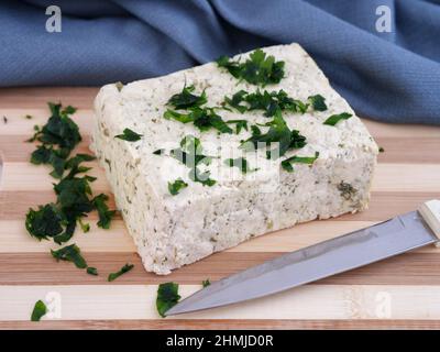 Ein Block Tofu mit etwas Petersilie darauf, der auf einem Schneidebrett liegt. Nahaufnahme. Stockfoto