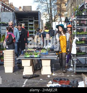 LONDON, ENGLAND - 12. Oktober 2018 Menschen kaufen Blumen auf dem Columbia Road Flower Market. Zwei hell gekleidete Mädchen gehen an Blumenvorführungen vorbei Stockfoto