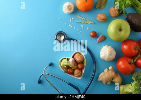 Natürliche Ernährungsmedizin mit gesunder Ernährung und Stethoskop auf blauem Hintergrund. Draufsicht. Horizontale Zusammensetzung. Stockfoto