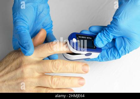 Sättigungsmessung einer 60-jährigen Asiatin. Die Hände eines Arztes tragen in medizinischen Handschuhen ein Pulsoximeter auf den Finger einer älteren Frau auf. Stockfoto