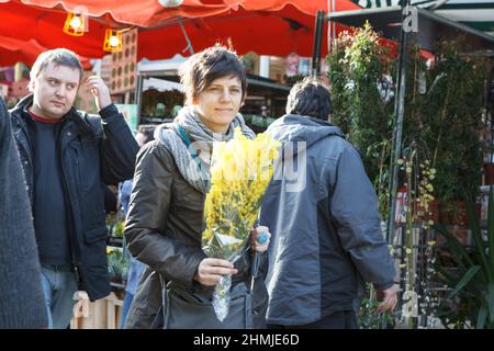 LONDON, ENGLAND - 12. Oktober 2018 Menschen kaufen Blumen auf dem Columbia Road Flower Market. Die Frau mit gelbem Bouquet von Mimosen gehen vorbei Displays wi Stockfoto