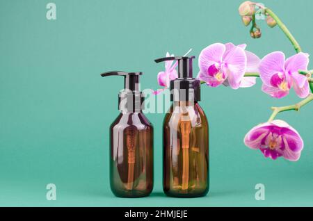 Kosmetikflaschen mit Spender auf grünem Hintergrund mit Orchideenblumen Stockfoto