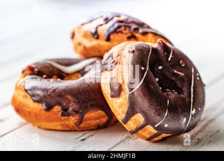 Drei Donuts in Schokolade auf einem weißen Holztisch, Nahaufnahme selektiver Fokus Stockfoto