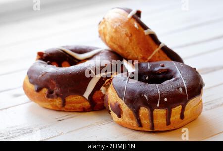 Drei Donuts in Schokolade auf einem weißen Holztisch, Nahaufnahme selektiver Fokus Stockfoto