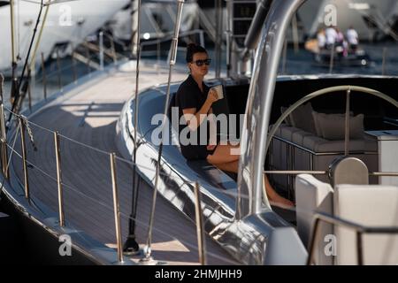 Monaco, Monte-Carlo, 28. September 2017: Mädchen in Sonnenbrillen sitzt auf dem Sofa der Segelyacht mit Tasse, Yachtmakler, Teilnehmer der größten Stockfoto